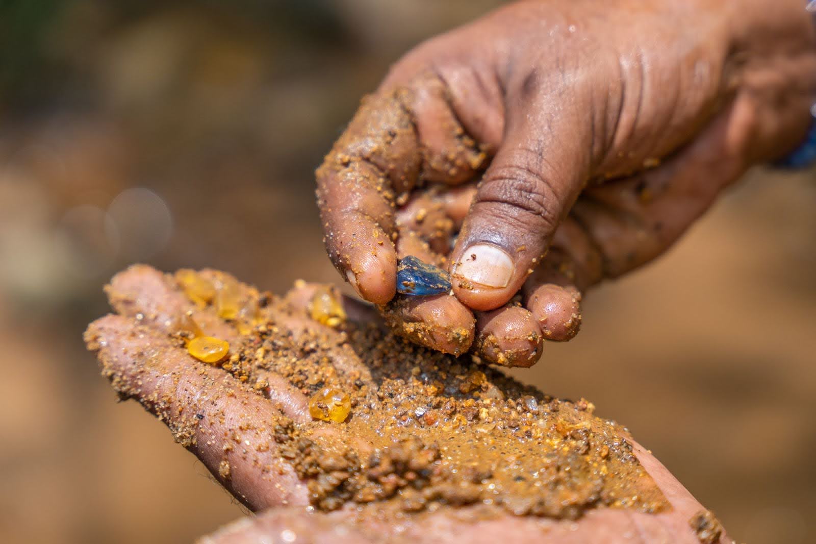 Man selecting yellow and blue gemstone roughs from illam-rich gravel using his hands with leftover, heavier material left on his palm